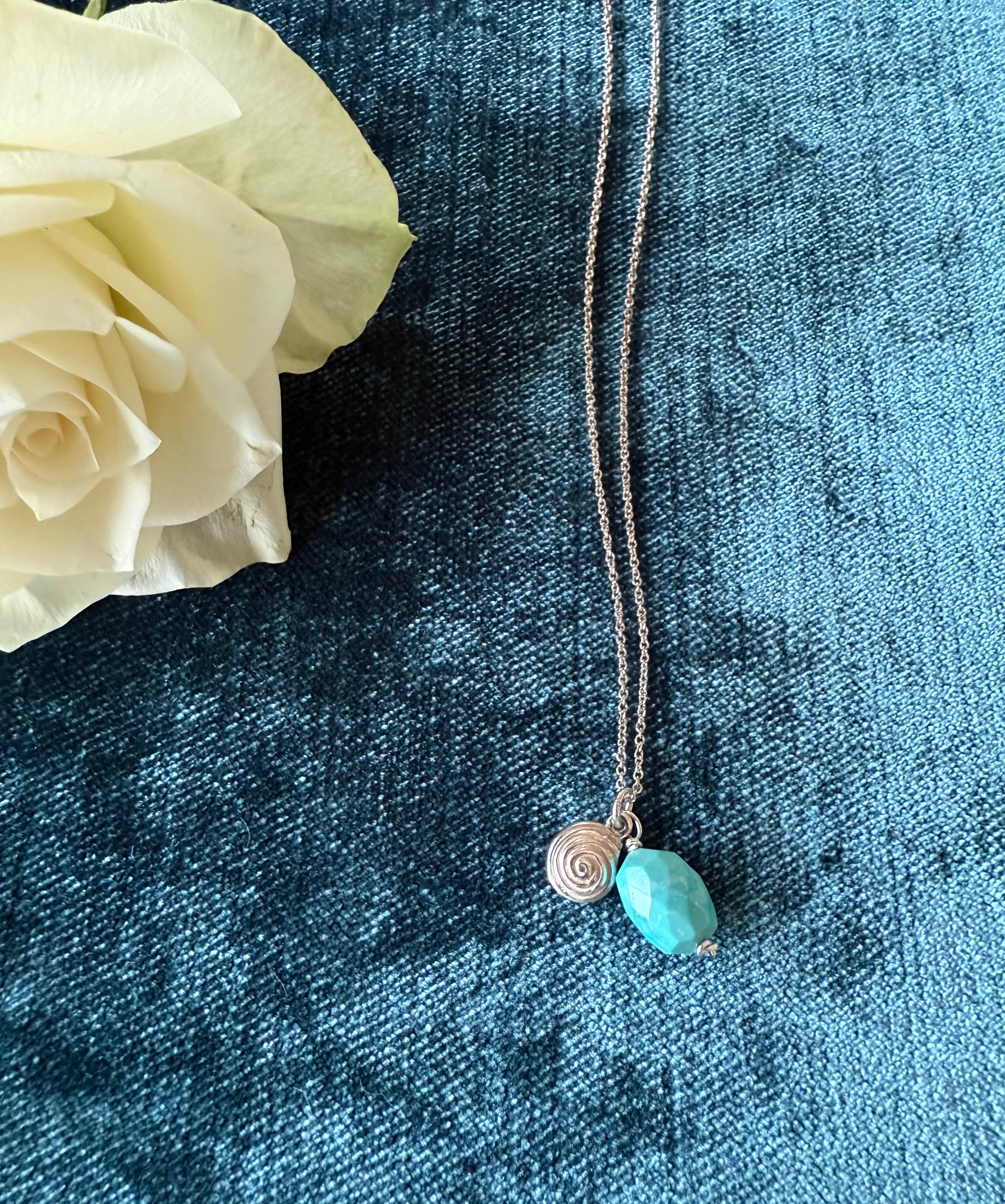 Silver spiral pendant with turquoise stone charm by Chorthip, showcasing a detailed silver design and vibrant turquoise pendant.