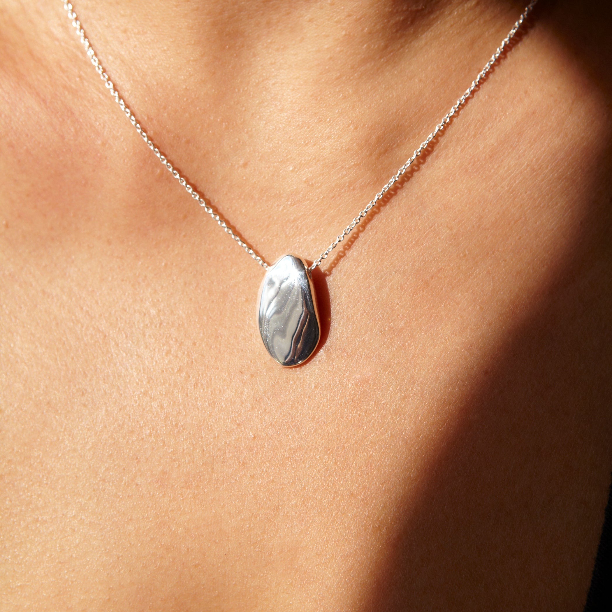 Close-up of Chorthip Pebble Stone Pendant showing smooth, rounded pebble design with a sleek silver bail on a plain background.