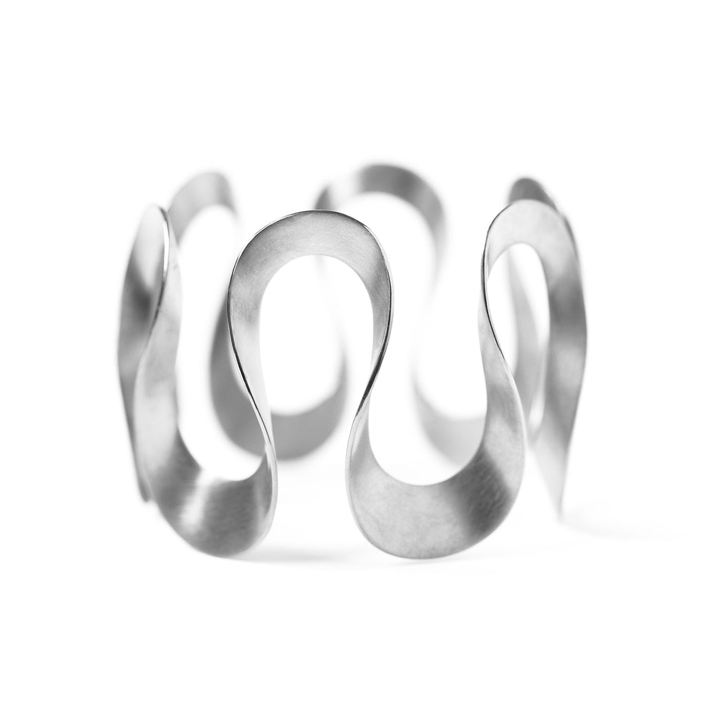 Silver infinity bangle by Chorthip featuring sleek, polished design with an infinity symbol in the center.